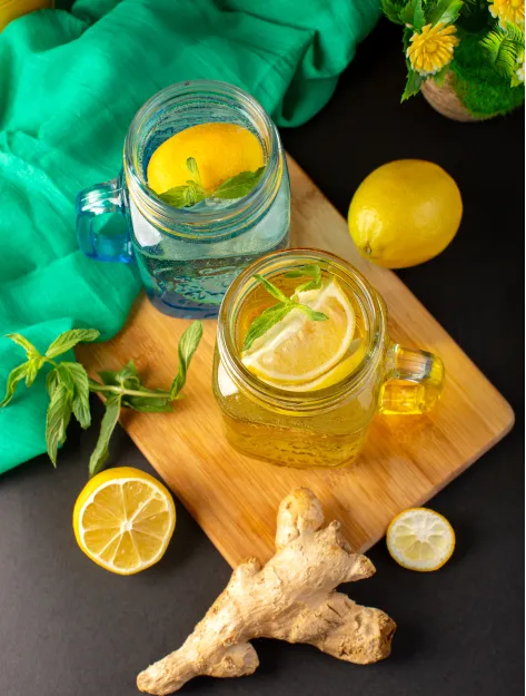 Two glass mason jars of iced lemon ginger tea with fresh mint sprigs.